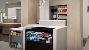 A hotel reception area with a minibar stocked with snacks and beverages, a counter with a sign, and a wall-mounted television. - Hilton Garden Inn Colorado Springs North Air Force Academy (Colorado Springs)