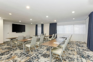 Un salón de conferencias con una larga mesa, sillas, un televisor de pantalla plana y una alfombra estampada.