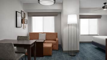 Habitación de hotel con cama, sofá, escritorio, silla, lámpara de pie y ventana.