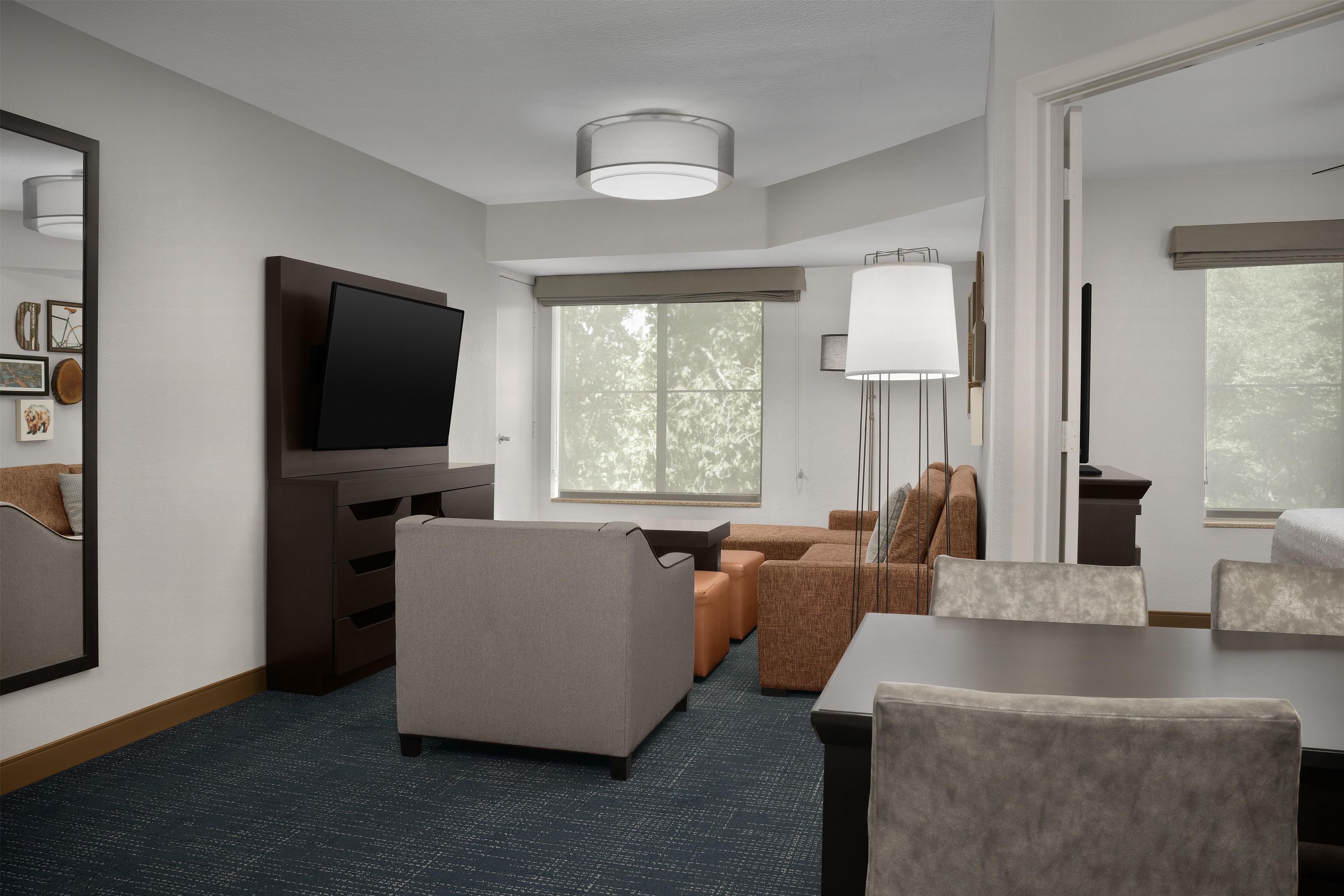 Habitación de hotel con televisor de pantalla plana, sofá, mesa de comedor y ventana grande.