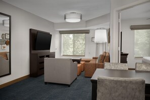 A hotel room with a flat-screen TV, a sofa, a dining table, and a large window. - Hampton Inn & Suites Denver Tech Center (Denver)