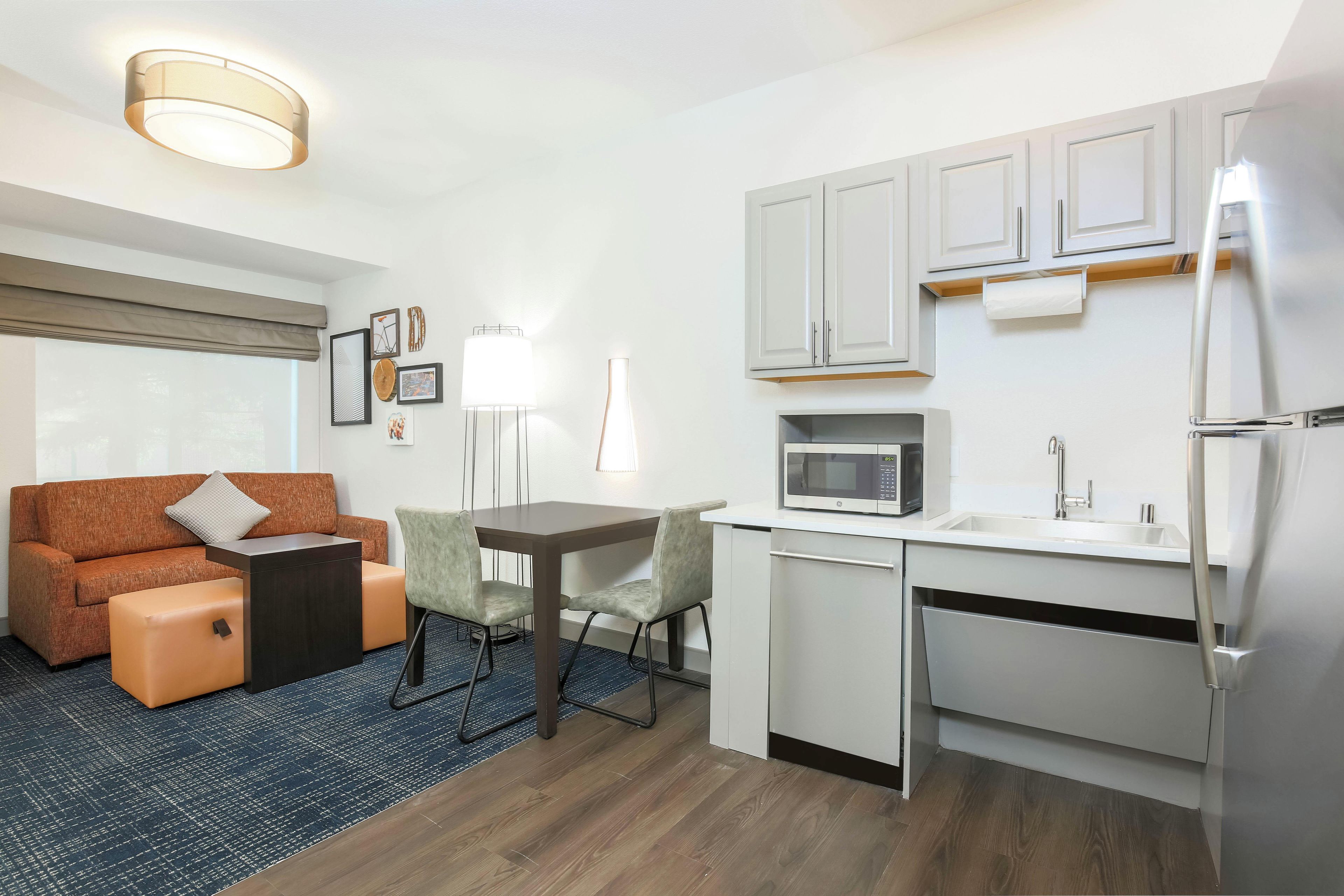 A compact living space with a kitchenette, a sofa, a dining table, and a lamp.