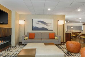 A modern living room with a fireplace, a sofa with orange cushions, a coffee table, and a large painting on the wall. - Hampton Inn & Suites Denver Tech Center (Denver)