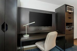 A hotel room with a dark wood desk, a flat-screen TV, a desk lamp, a chair, and a built-in microwave.