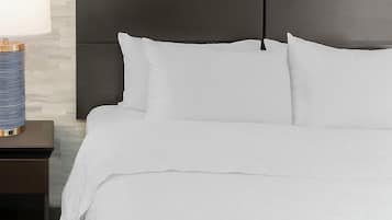 A neatly made bed with white bedding, a dark headboard, and a bedside table with a lamp.