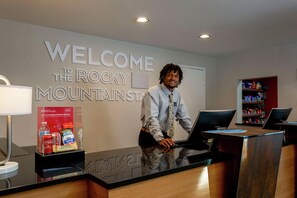 A reception desk with a 'WELCOME TO THE ROCKY MOUNTAIN' sign, a laptop, a watch, and a display of local snacks. - Hampton Inn & Suites Denver Tech Center (Denver)
