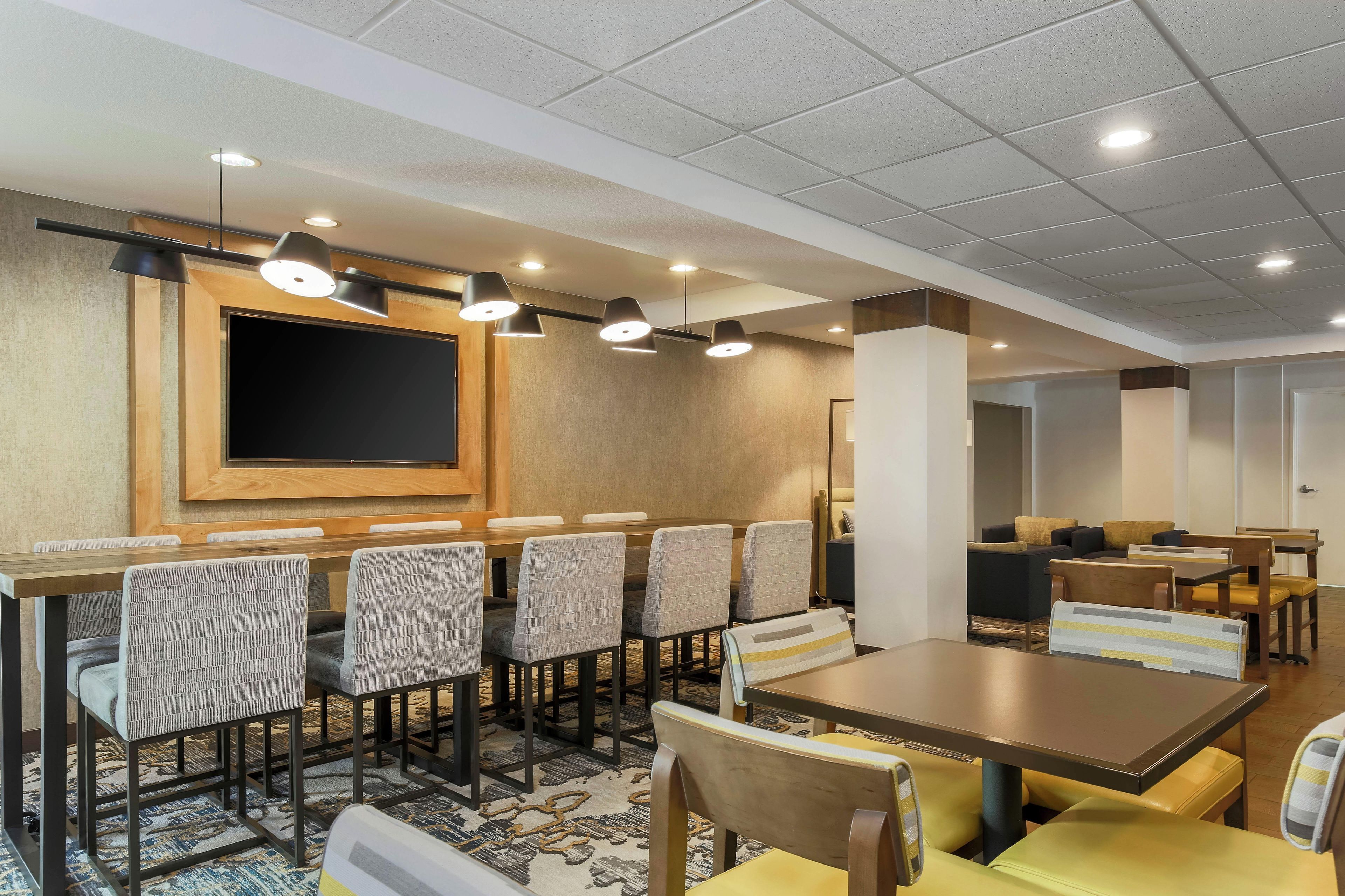 A hotel dining area with a long table, multiple chairs, and overhead lighting.