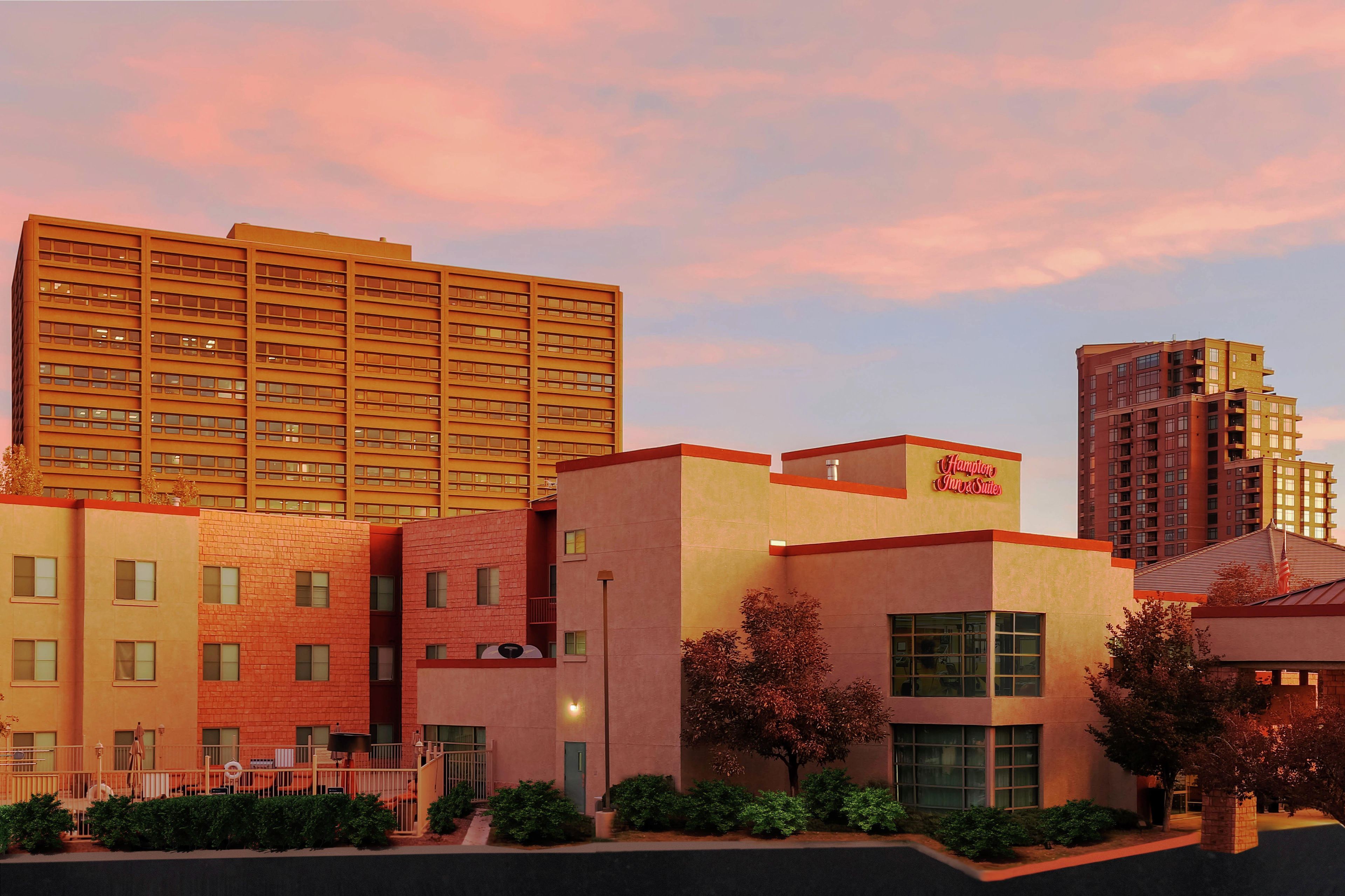 A hotel with multiple floors, a prominent sign for Hampton Inn & Suites, and a parking lot with a fence.