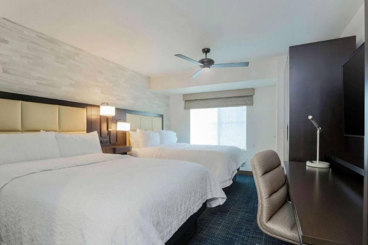 Habitación de hotel con dos camas, ventilador de techo, escritorio con lámpara y televisión.