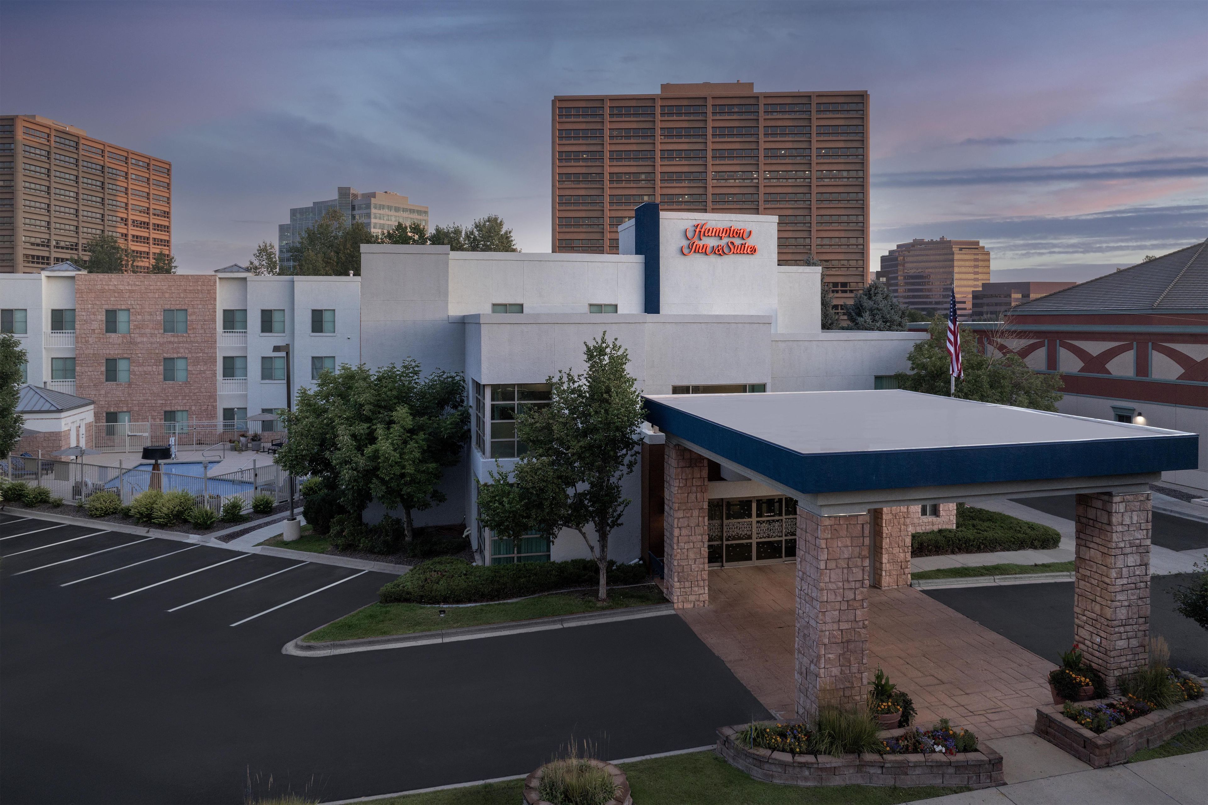 A hotel with a flat roof, a parking lot, and a large building in the background.