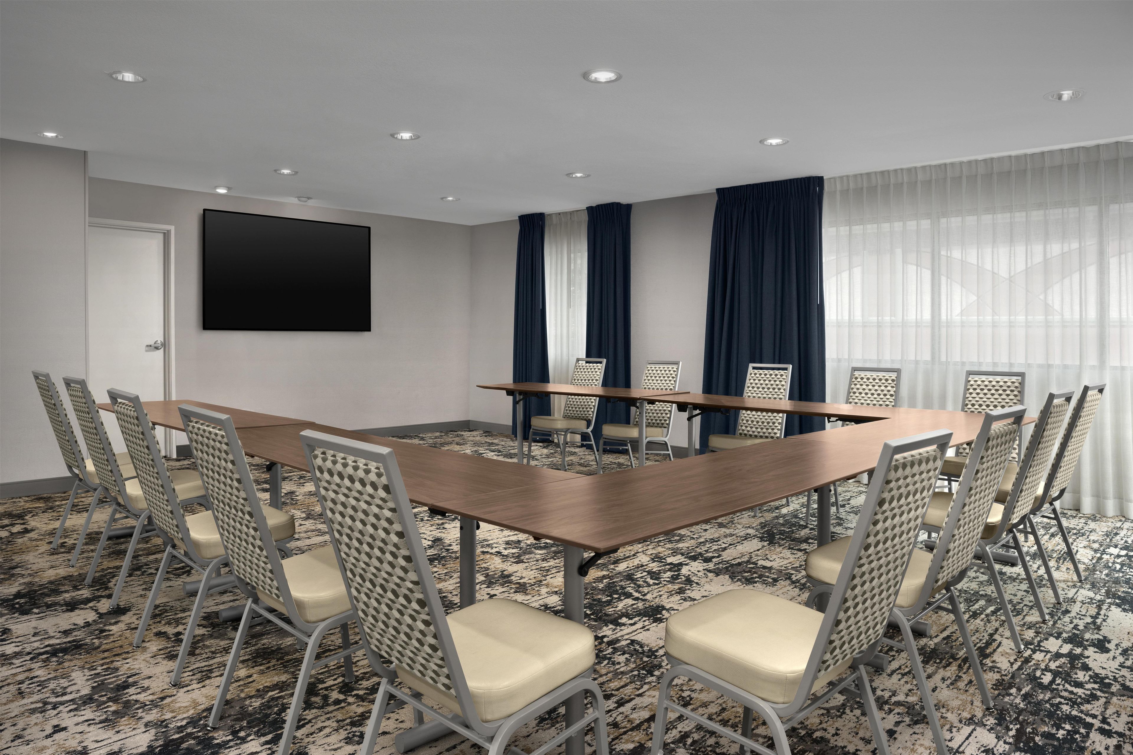 A conference room with a large table, chairs, a flat-screen TV, and a patterned carpet.