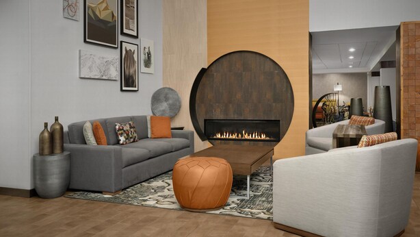 Un salon moderne avec une cheminée, des canapés gris et un pouf rond.