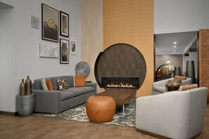 A modern living room with a fireplace, grey sofas, and a round ottoman.