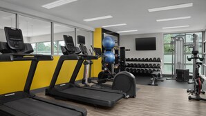 Une salle de sport équipée de tapis de course, d’une machine de musculation et d’haltères.