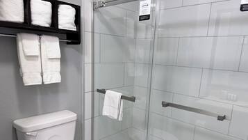Casa de banho com sanita, cabine de duche em vidro e prateleira com toalhas dobradas.
