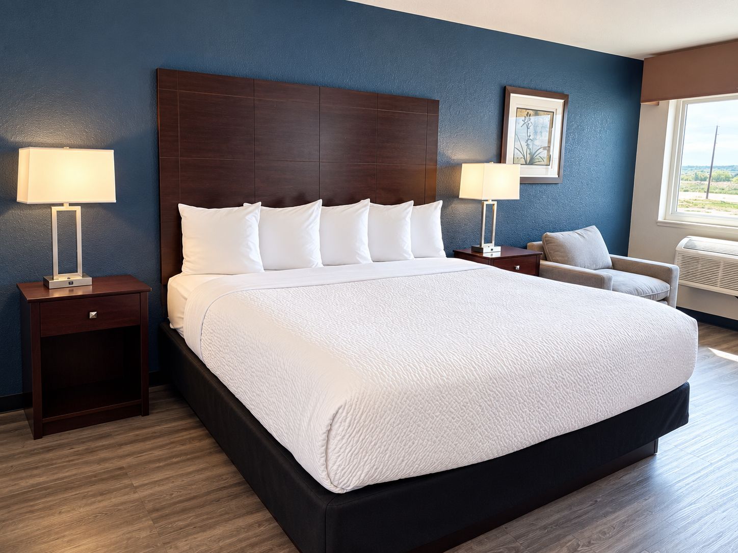 A hotel room with a large bed, two bedside tables with lamps, a chair, and a window.
