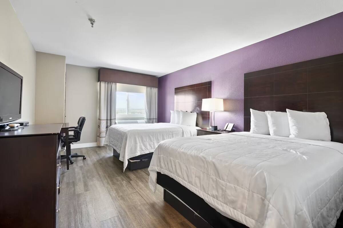 A hotel room with two beds, a desk with a television, a chair, and a window with curtains.