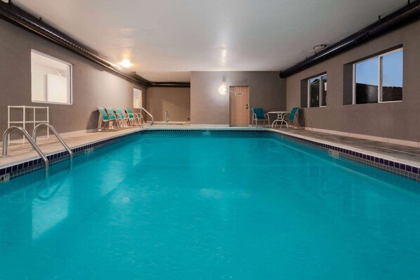An indoor swimming pool with clear blue water, surrounded by lounge chairs and a door. - Baymont by Wyndham Henderson Northeast Denver (Henderson)