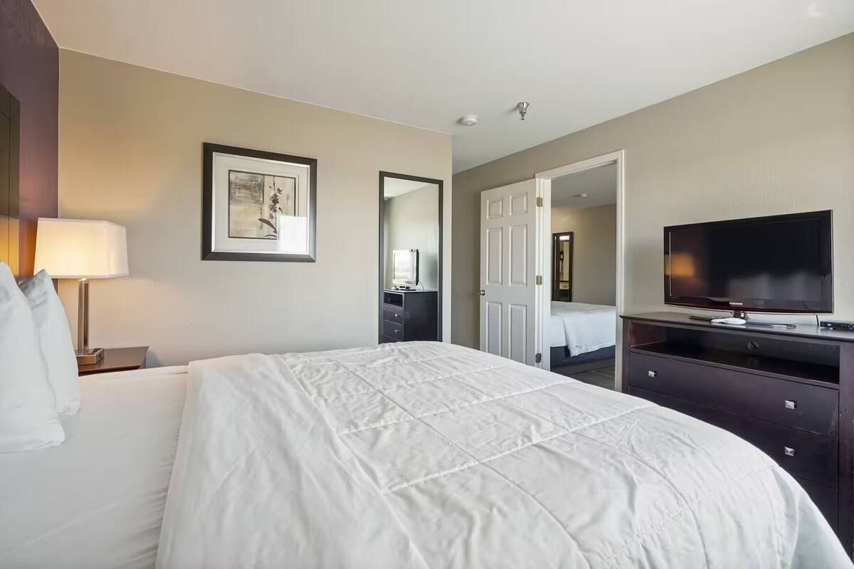 A hotel room with a bed, a TV, a dresser, and a lamp.