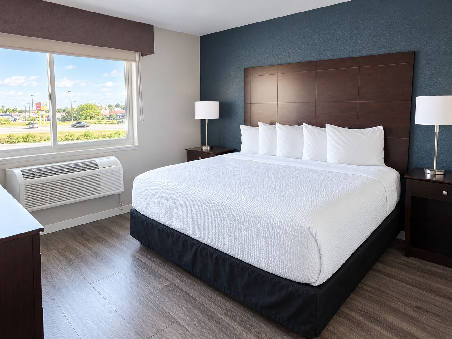 A hotel room with a large bed, two bedside tables, a window with a view, and a wall-mounted heater.