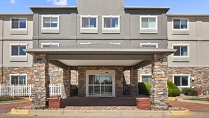A multi-story building with a covered entrance, stone pillars, and a white picket fence.
