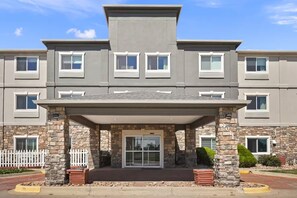 A multi-story building with a covered entrance, stone pillars, and a white picket fence. - Baymont by Wyndham Henderson Northeast Denver (Henderson)