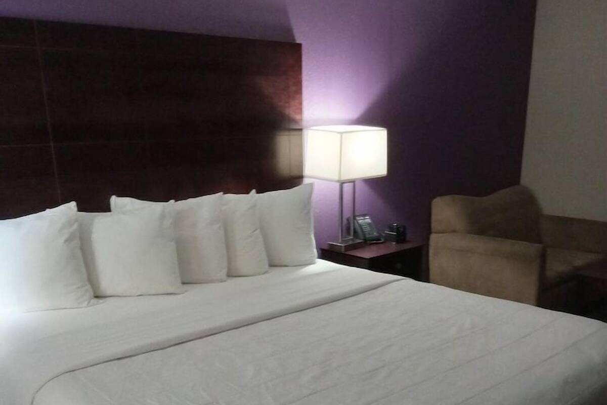 A hotel room with a large bed, a nightstand with a lamp, and a chair.
