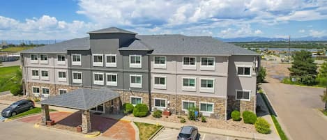A multi-story hotel with a covered entrance, parking lot, and a view of the surrounding landscape.