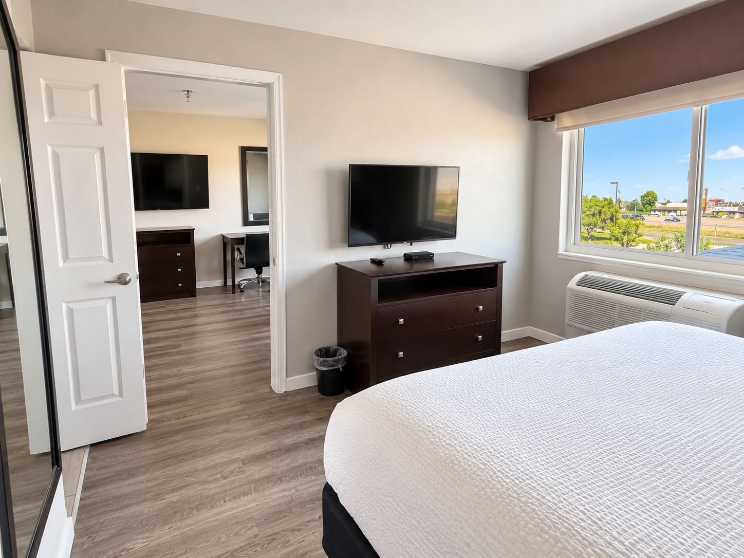 A hotel room with a bed, a TV, a desk with a chair, and a view of the outdoors.