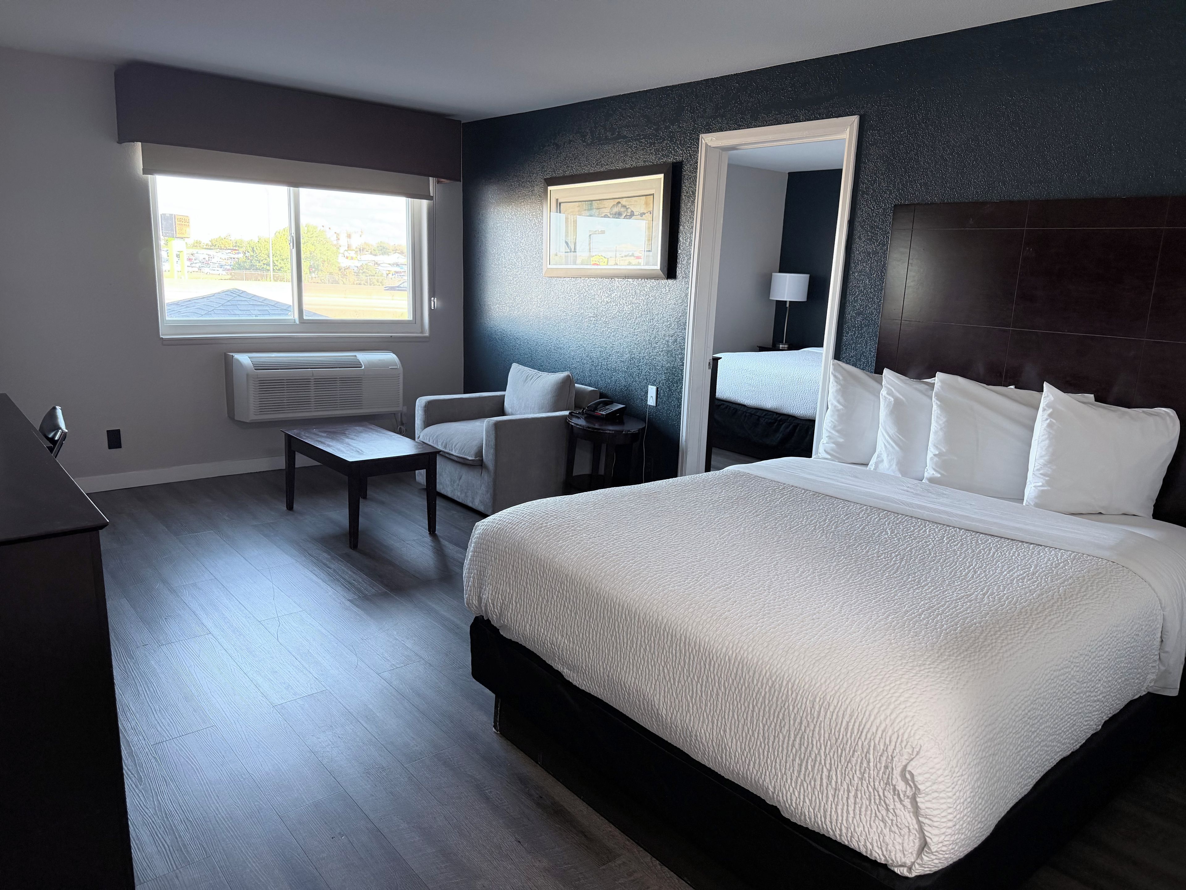 Quarto de hotel com uma cama grande, uma mesa, uma cadeira, janela com vista e espelho fixado na parede.