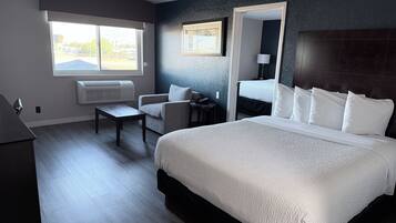 Quarto de hotel com uma cama grande, uma mesa, uma cadeira, janela com vista e espelho fixado na parede.