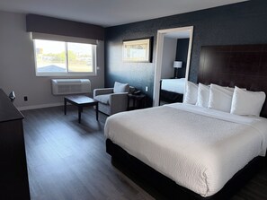 A hotel room with a large bed, a desk, a chair, a window with a view, and a wall-mounted mirror. - Baymont by Wyndham Henderson Northeast Denver (Henderson)