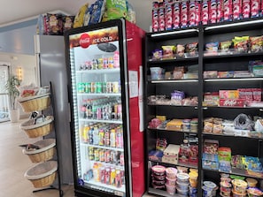 A vending machine stocked with beverages and snacks, adjacent to shelves with packaged goods.