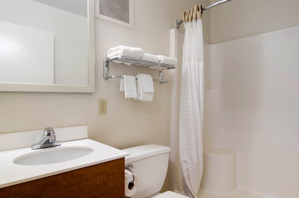 A bathroom with a sink, mirror, towel rack, toilet, and shower curtain. - HomeTowne Studios by Red Roof Denver - Thornton (Thornton)