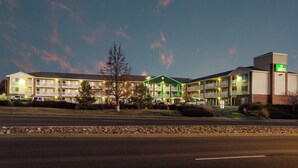 Un motel à plusieurs étages, doté d’un auvent vert, d’un parking et surplombant un ciel dégagé.