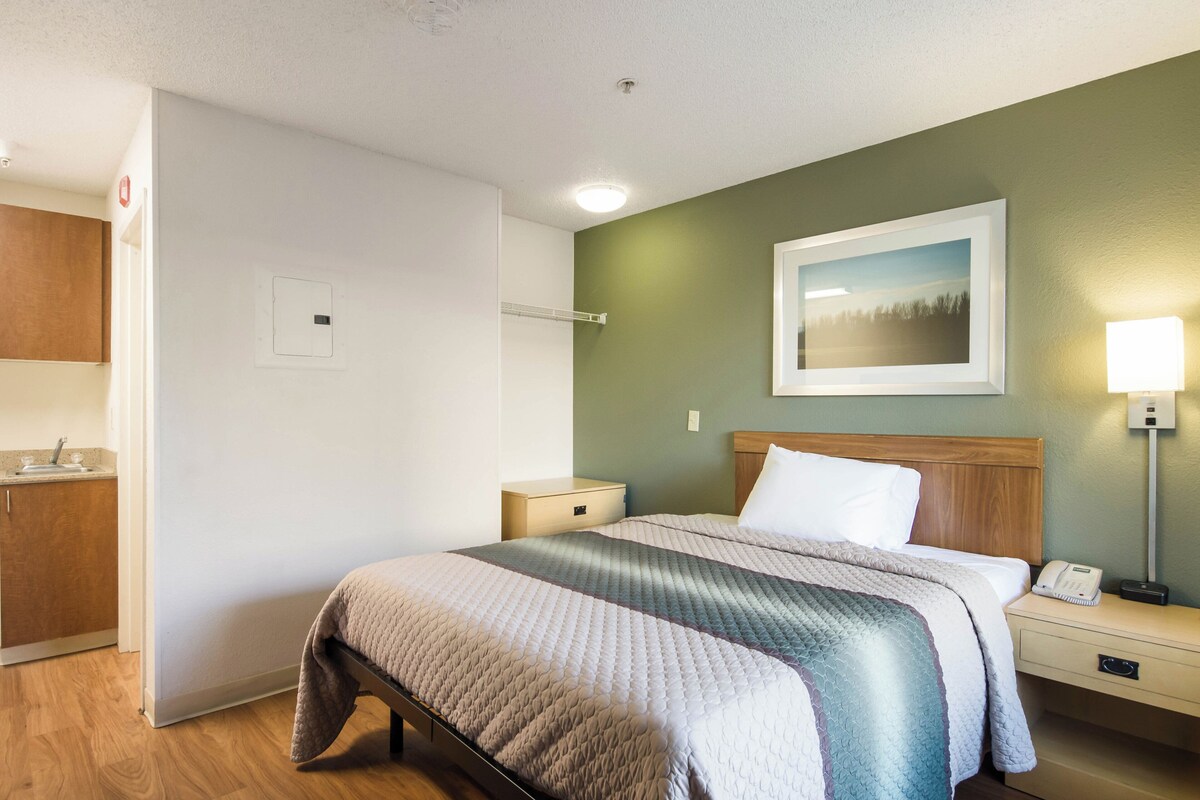 A hotel room with a bed, bedside table, nightstand, and a wall-mounted picture.