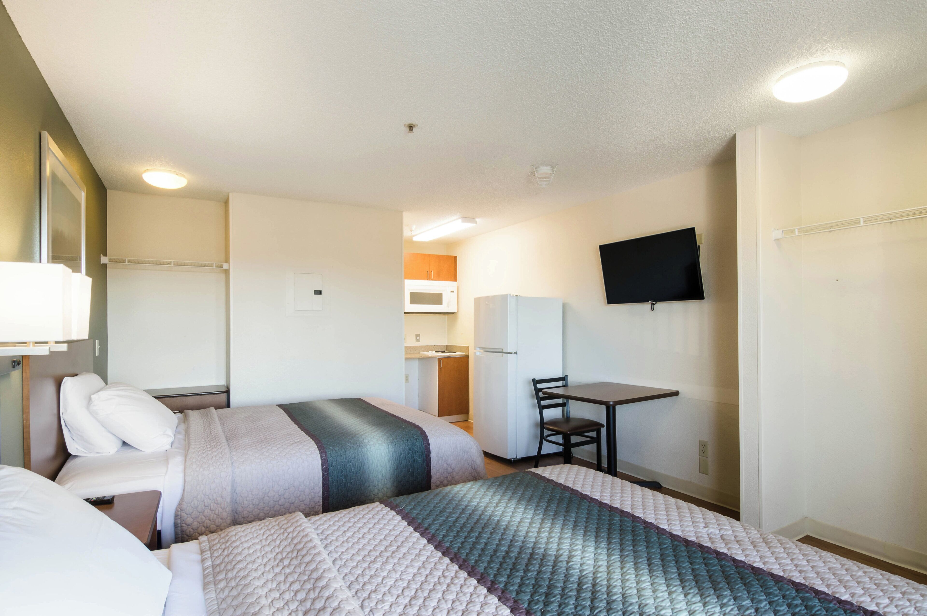 Habitación de hotel con cama, escritorio, silla, televisor y kitchenette.