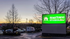 A sign for Home Towne Studios by RedRoof in a parking lot with trees and a sunset in the background. - HomeTowne Studios by Red Roof Denver - Thornton (Thornton)