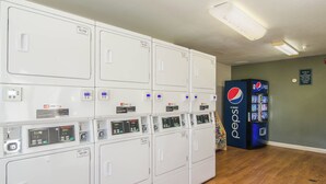 A laundry room with multiple washing machines and dryers, a vending machine, and a wall sign. - HomeTowne Studios by Red Roof Denver - Thornton (Thornton)