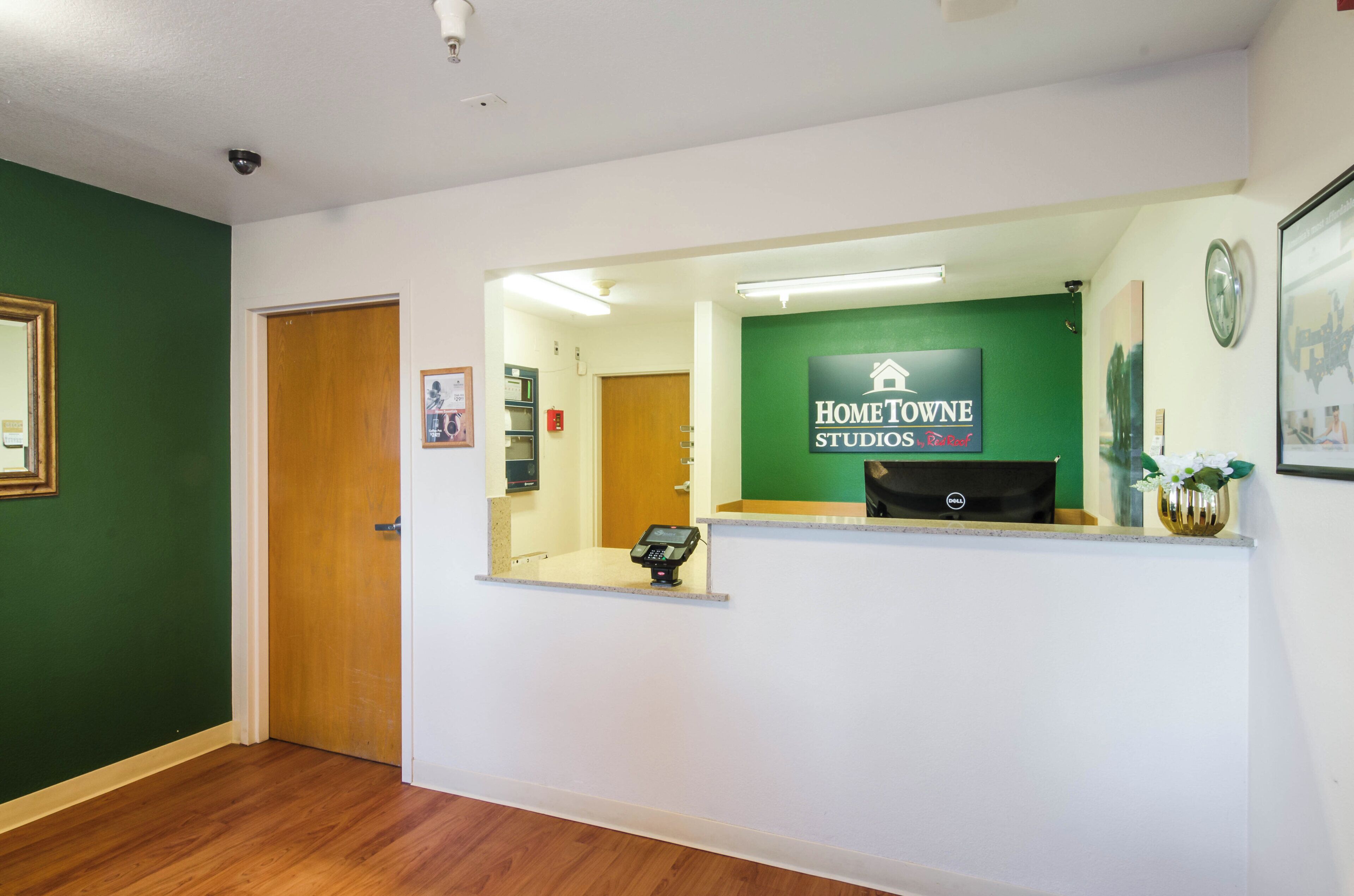 Un mostrador de recepción con un cartel de Home Towe Studios by Red Roof, una puerta de madera y un cuadro en la pared.