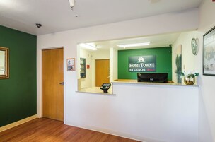 Un mostrador de recepción con un cartel de Home Towe Studios by Red Roof, una puerta de madera y un cuadro en la pared.