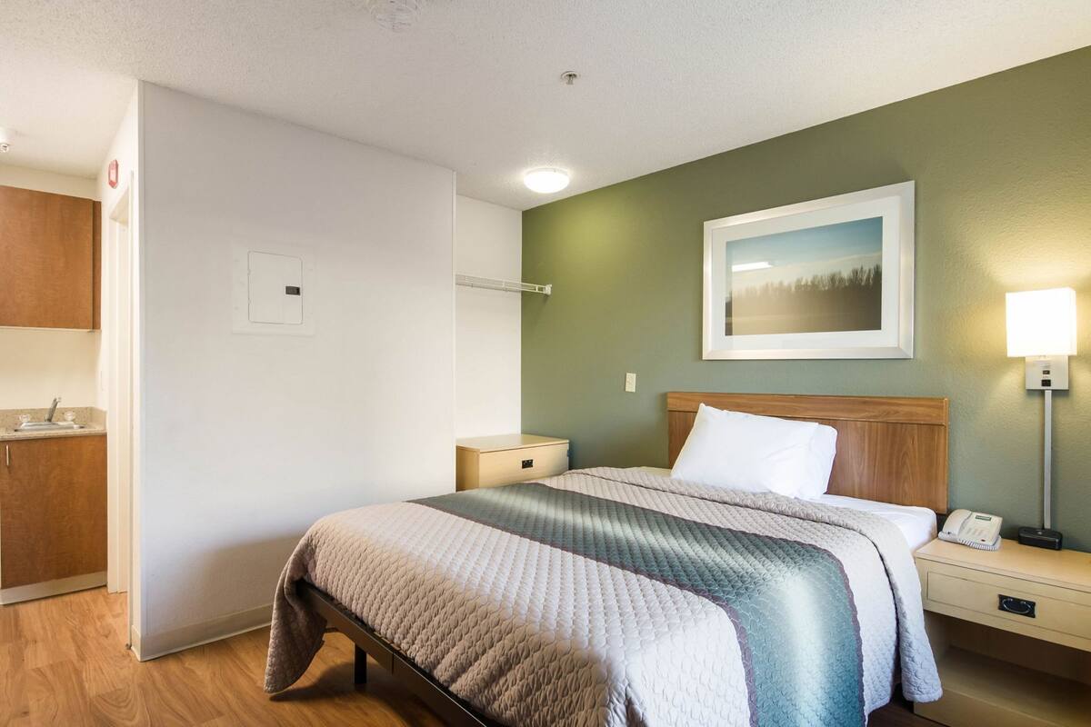 Ein Hotelzimmer mit Bett, Nachttisch, Lampe und einem Gemälde an der Wand.
