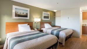 A hotel room with two beds, a nightstand with a lamp, and two framed pictures on the wall. - HomeTowne Studios by Red Roof Denver - Thornton (Thornton)