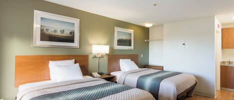 Ein Hotelzimmer mit zwei Betten, einem Nachttisch mit Lampe und zwei gerahmten Bildern an der Wand.