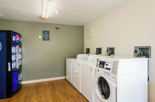 Un cuarto de lavandería con una máquina expendedora, un cartel y lavadoras apiladas.
