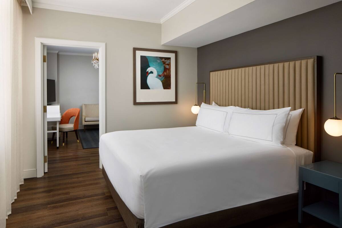 Habitación de hotel con una cama grande, un escritorio con silla, televisión y un cuadro en la pared.