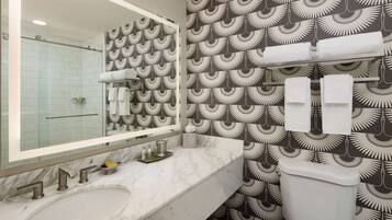 Un baño con lavamanos de mármol, un espejo grande, inodoro y papel tapiz estampado.