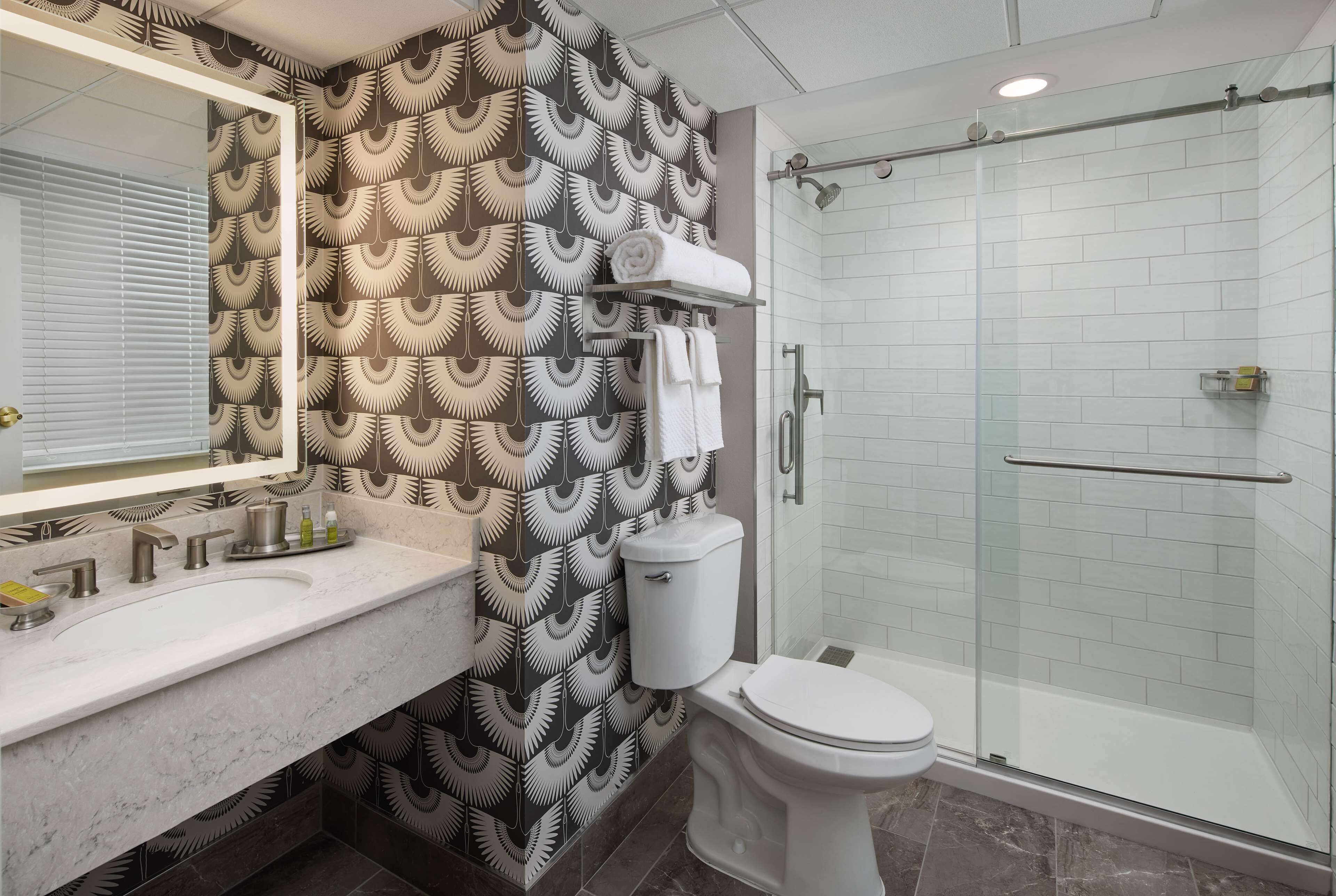 Une salle de bain avec un mur à motifs, un lavabo blanc, des toilettes et une douche à parois de verre.
