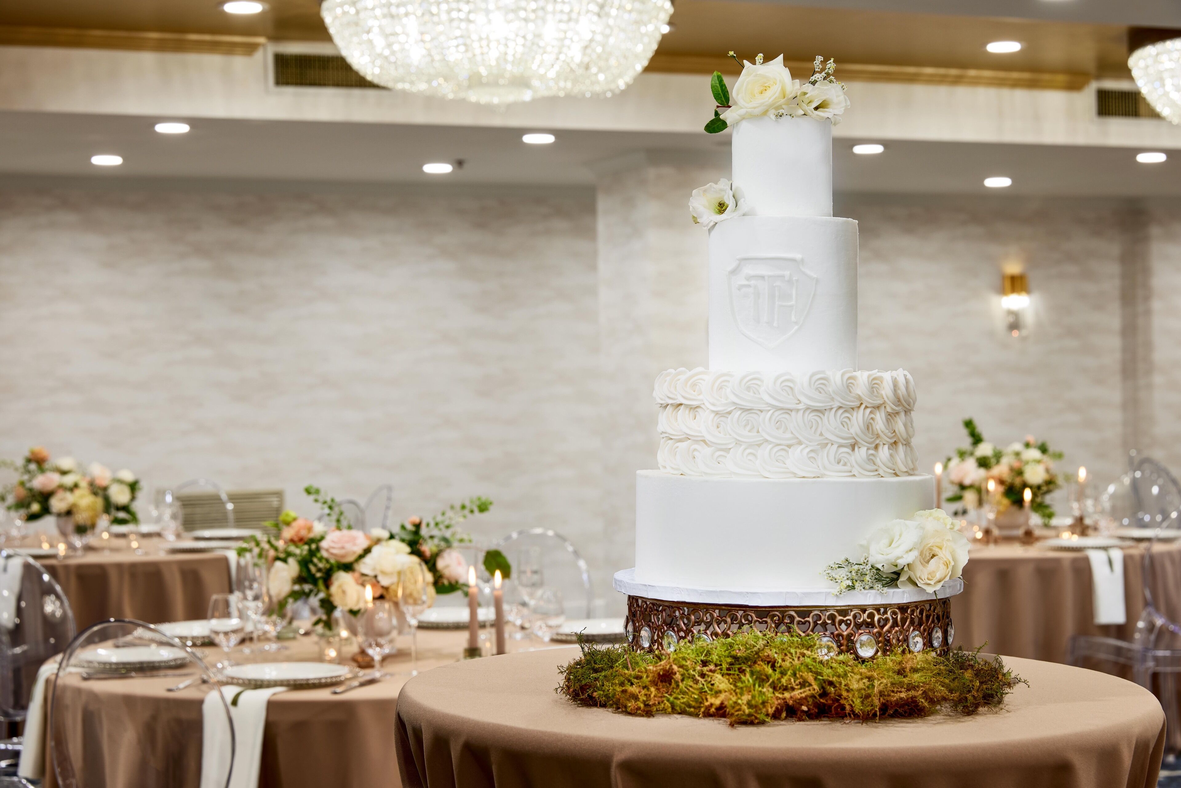 A multi-tiered white wedding cake with floral decorations on a table in a banquet hall.