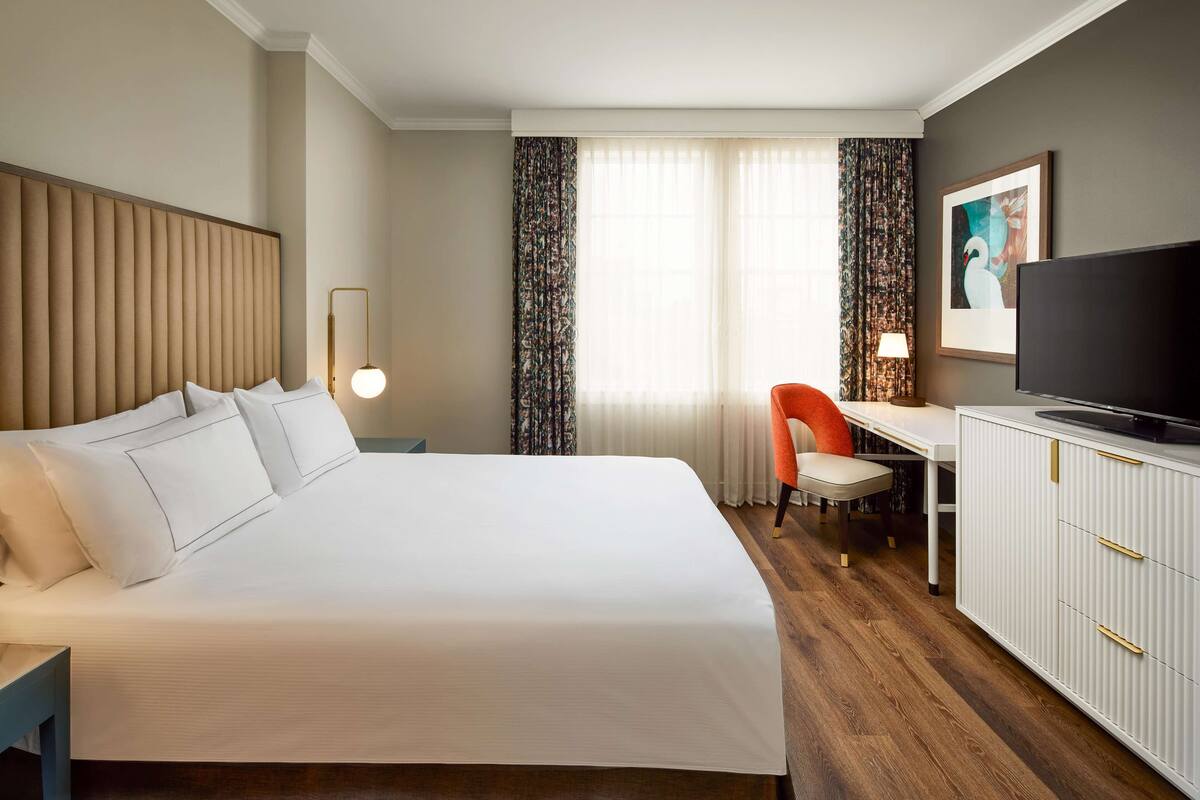 Una habitación de hotel con una cama grande, un escritorio con una silla, un televisor y un armario.